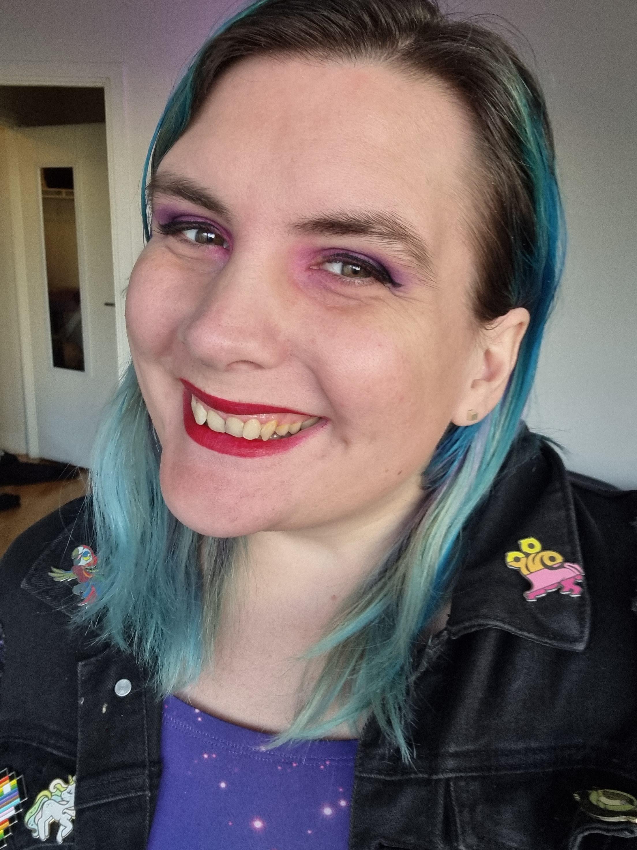 Ash smiling joyfully with long bluegreen hair and pink and purple eyeshadow