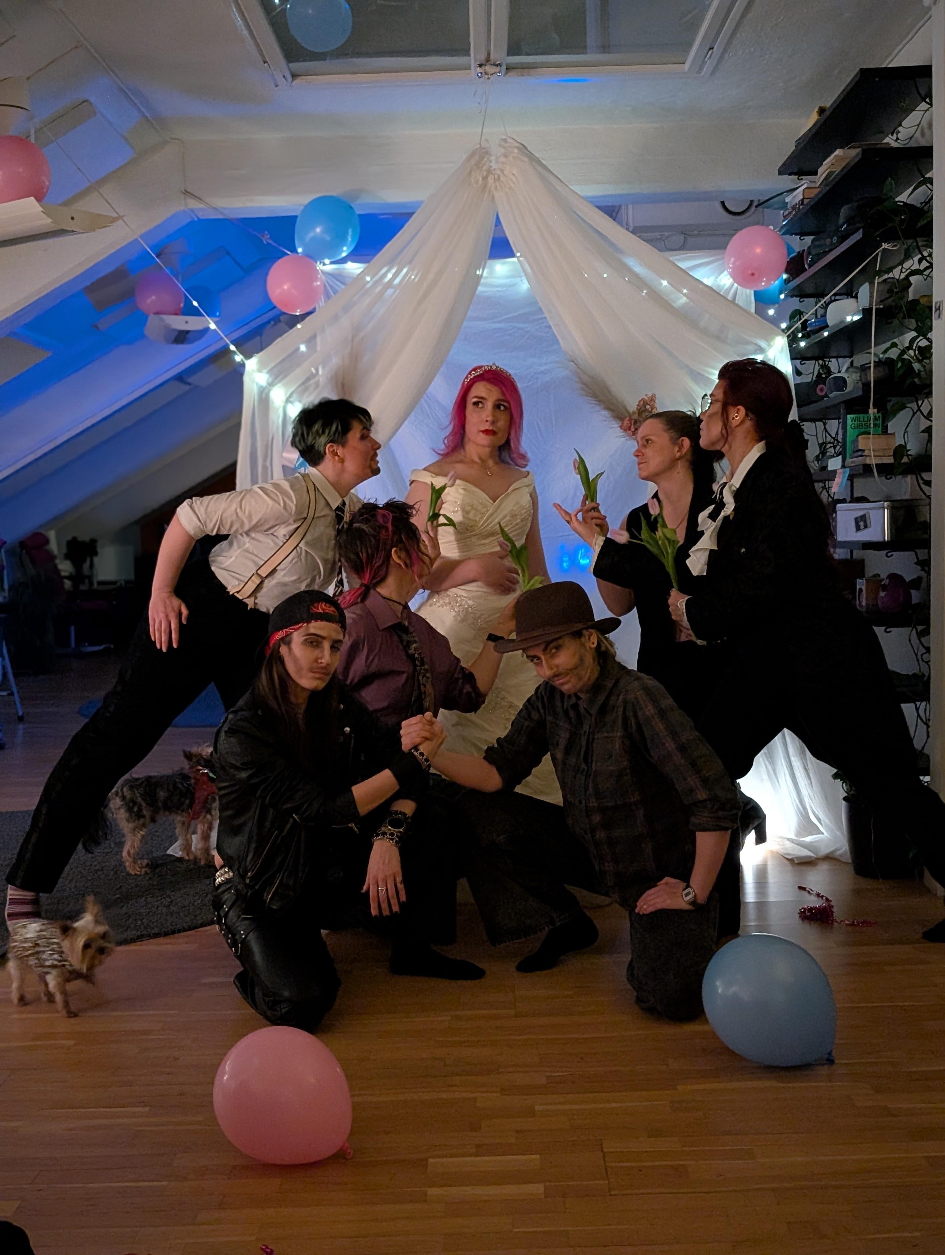hA photo of Ash in a wedding dress and tiara surrounded by a harem of drag kings doting over her