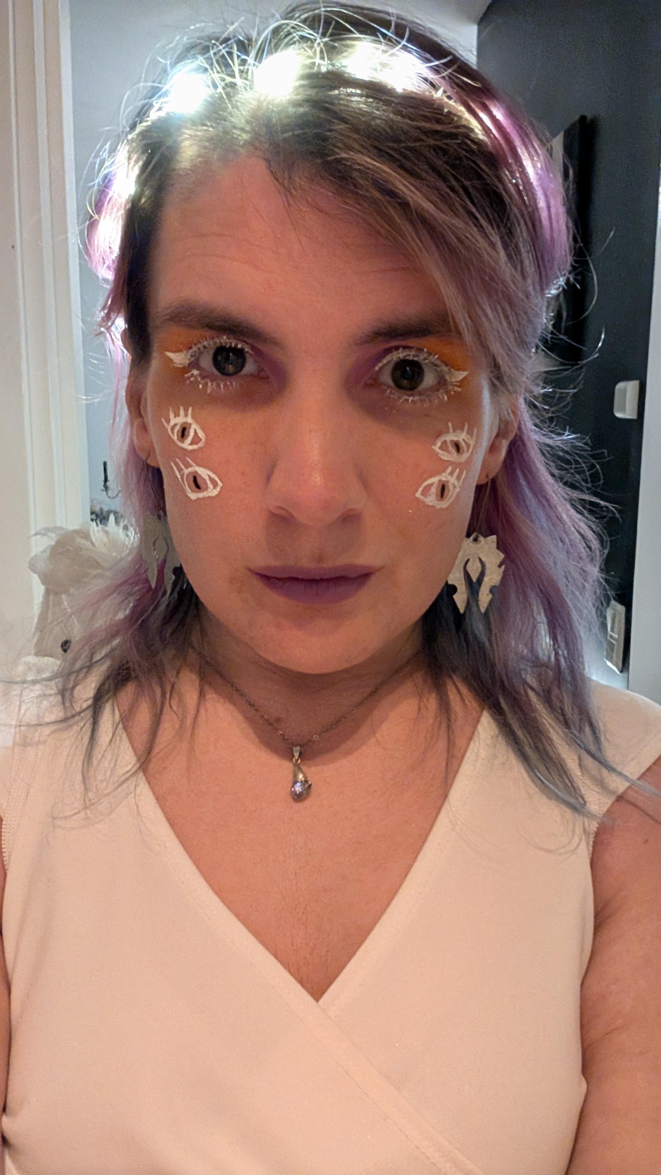 Closeup of Ash's makeup featuring white eyeliner and mascara, eyeshadow blending from lilac to gold like the dawn, and four extra eyes drawn down her cheeks.