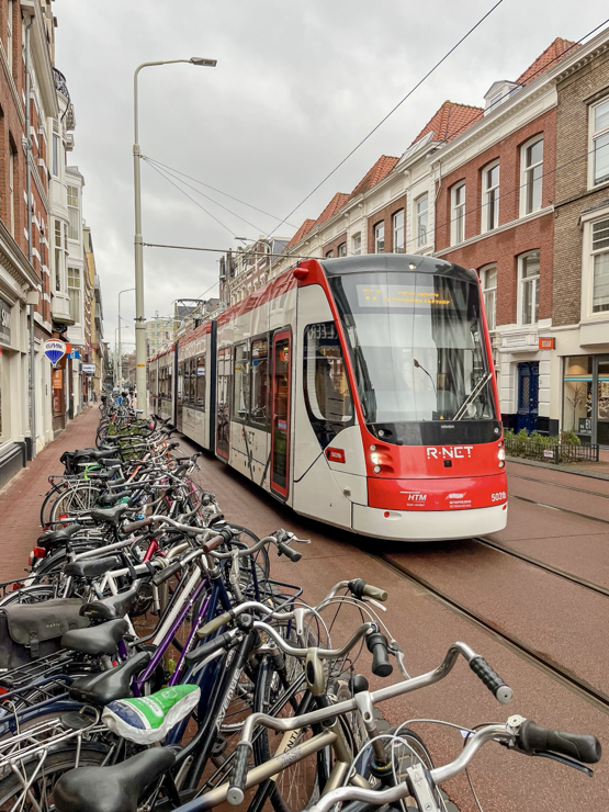 A modern red and white tram glides along a red asphalt car-free shopping street lined with brick buildings and dozens of parked bikes in The Hague.