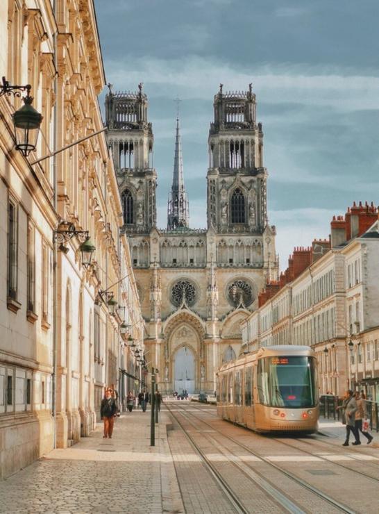 A golden-hued tram on a car-free street in Orléans France, against a backdrop of similarly-colored townhouses and the city’s Gothic cathedral
