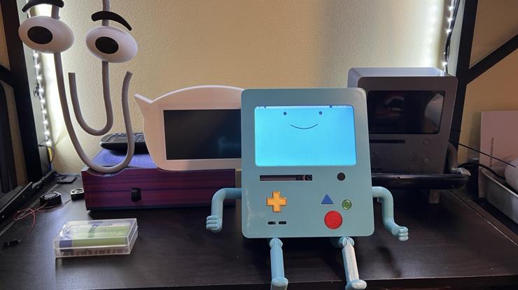 Image of the teal BMO-AI robot with predecessor robots like ClippyGPT in the background.