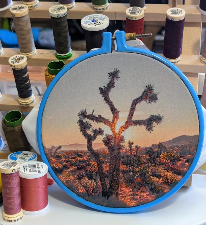An embroidery hoop holding material on which I'm stitching a landscape of Joshua Tree at sunset.