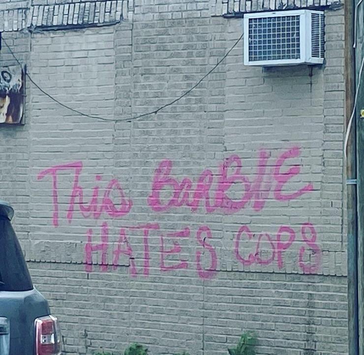 "This barbie hates cops" written on a wall with pink spray paint