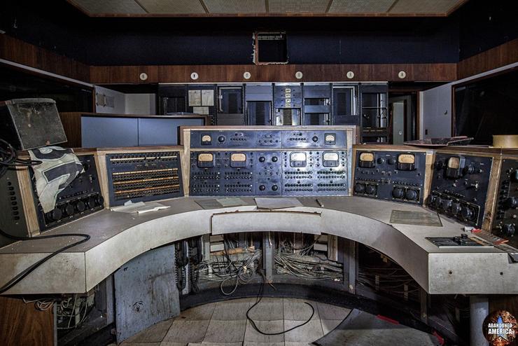 A large half-circle shaped radio console covered with gages and wires in a darkened booth