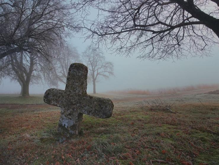 Photo of a stone cross framed by barren trees. About to be swallowed by fog.
