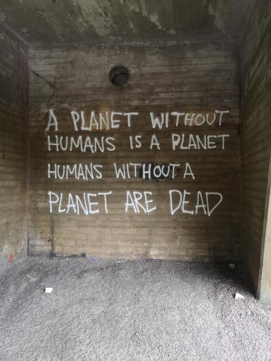 "A planet with humans is a planet humans without are planet a dead" written on a wall with white spray paint